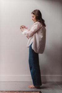 Smiling mother holding her newborn baby girl in a naturally lit nursery during a lifestyle newborn photoshoot with Zur Photography.