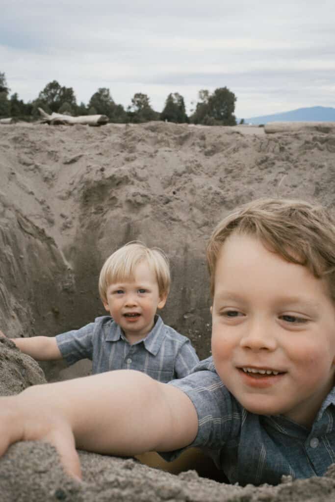 Two kids playing in a sand hole and laughing on Kitsilano Beach