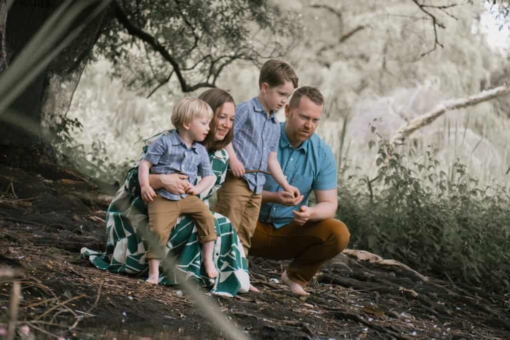 A young family explores the wildlife by a pond, with the parents showing their children the different plants and creatures.